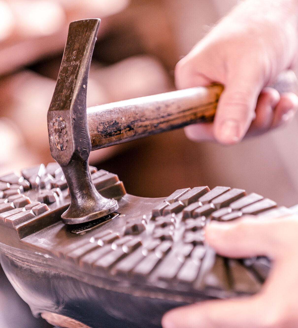 Schuhmacher bearbeitet die profilierte Gummisohle eines robusten Schuhs mit dem Hammer.